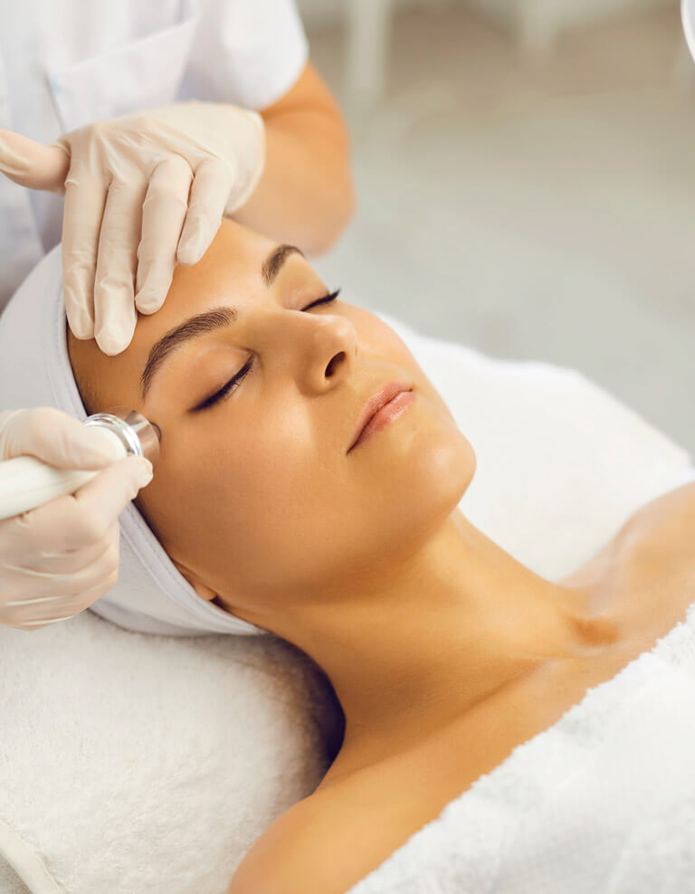 A woman wrapped in white towels lays down while receiving aesthetic laser therapy.