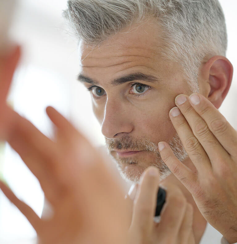 Middle-aged man inspects his face in the mirror.