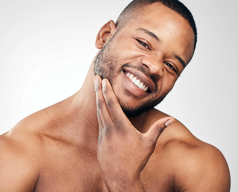 A smiling black man with nice skin. He is rubbing his chin.
