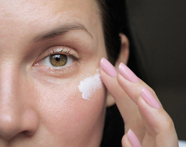 A woman applies a retinol cream under her eyes.