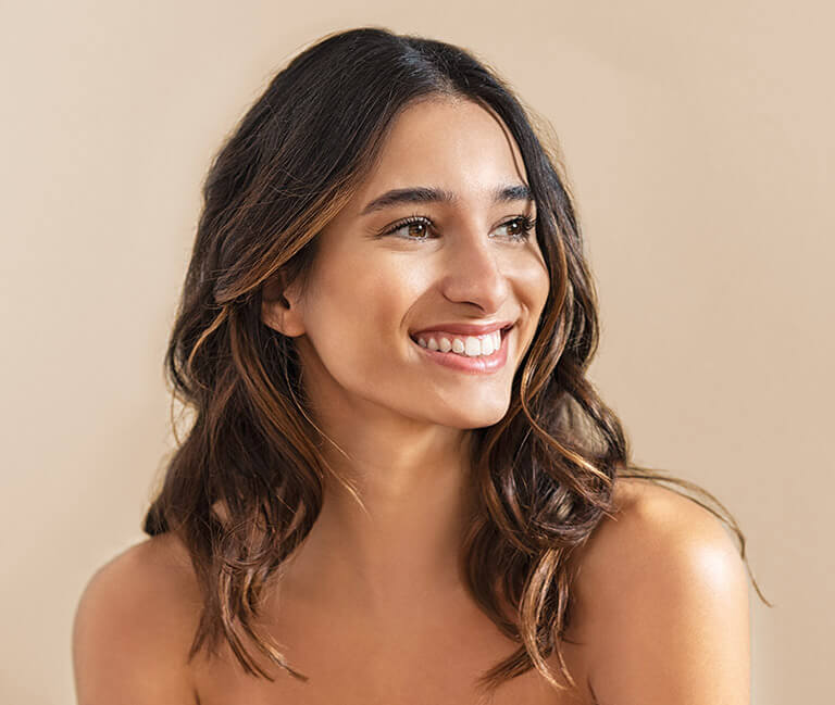 A smiling brunette woman looks off camera. Her skin is flawless.