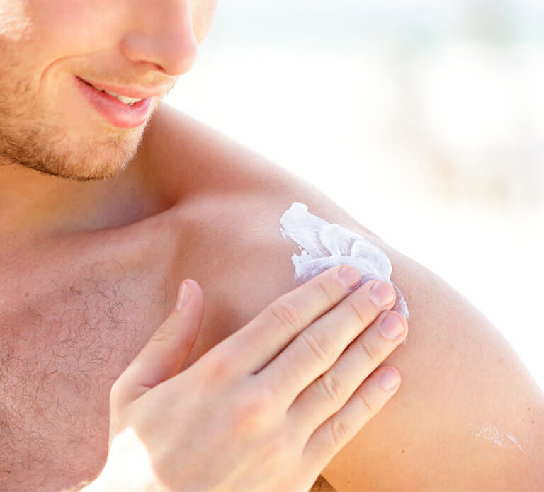 Unidentifiable man applies sunscreen to his shoulder.